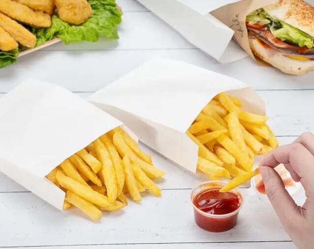 Punga hartie alba cu cartofi prajiti si sos ketchup pe masa, ideal pentru servirea produselor prajite.