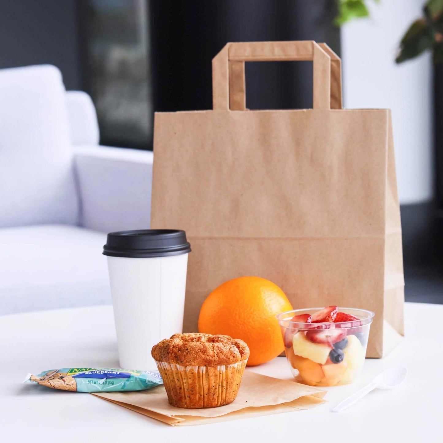 Punga hartie natur cafea 20x9x25cm cu micul dejun, includând o cafea, un muffin, un fruct și un pachet de snack.