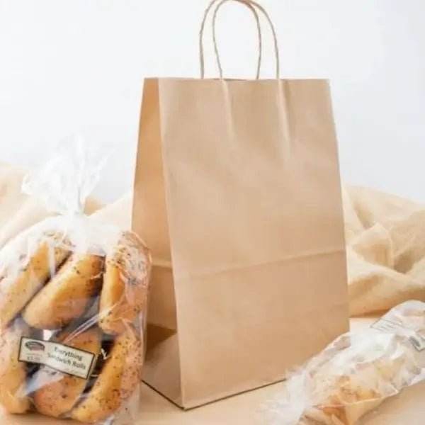 Punga hartie natur cu maner sfoara 20x9x25cm pe masa, alaturi de produse de patiserie ambalate.
