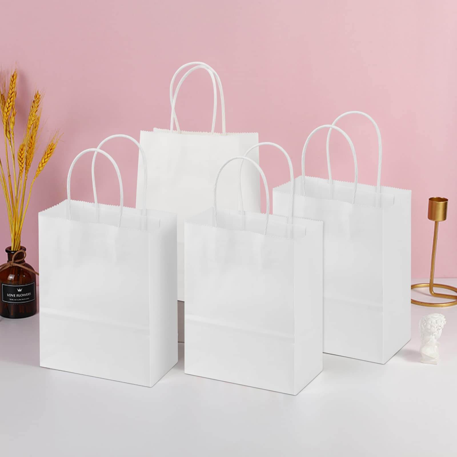 Set of four white paper bags with twisted handles on a stylish table background.