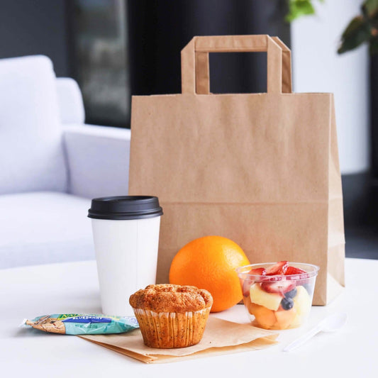 Punga hartie natur cafea 20x9x25cm cu micul dejun, includând o cafea, un muffin, un fruct și un pachet de snack.