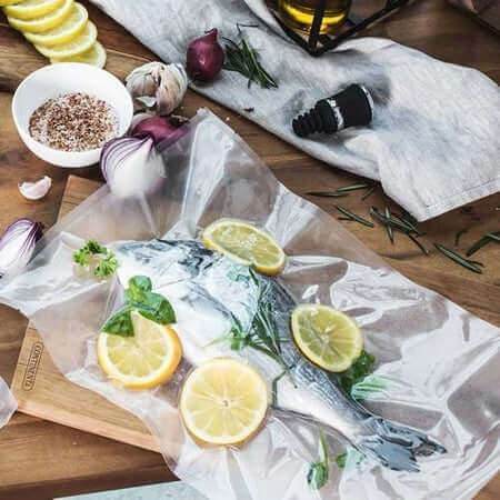 Pungi vidat gofrate 400x600 used for vacuum sealing fish with lemon and herbs on wooden board.